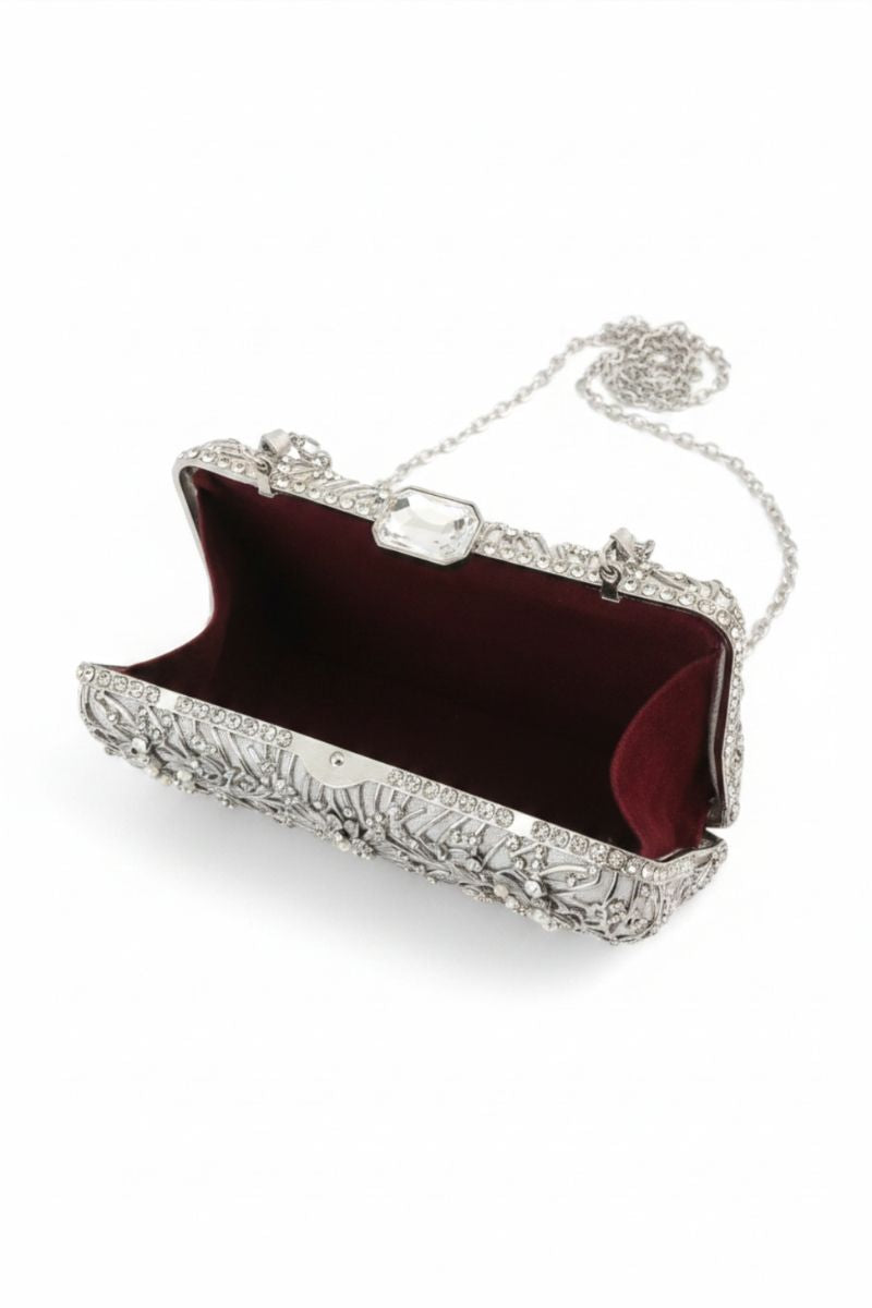 An ornate silver clutch purse with a textured, embellished exterior, an open burgundy velvet interior, and a delicate silver chain strap, shown on a plain white background.